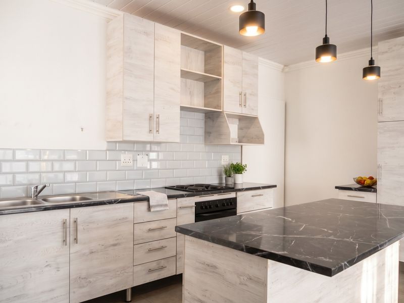 Modern kitchen featuring light wood-grain cabinetry, black marble-effect countertops, a central island, subway tile backsplash, and integrated stainless steel appliances.