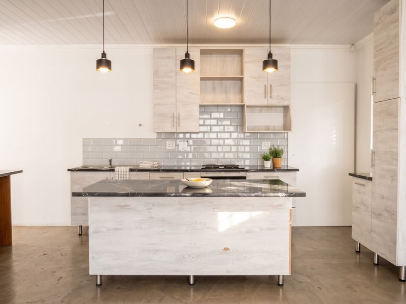 Modern kitchen featuring light wood-grain cabinetry, a marble-look island, subway tile backsplash, and industrial pendant lighting over a polished concrete floor.