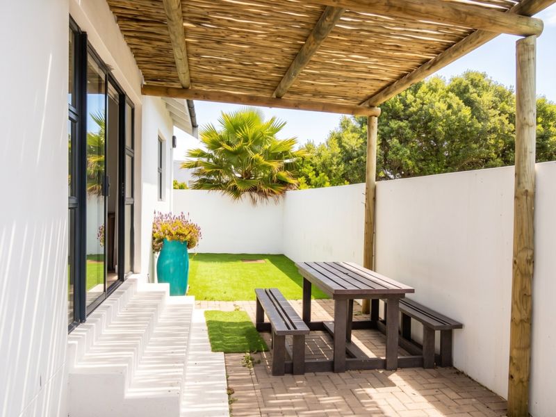 A well-maintained outdoor patio area featuring a timber pergola, paved flooring, and direct access to the garden through sliding glass doors.