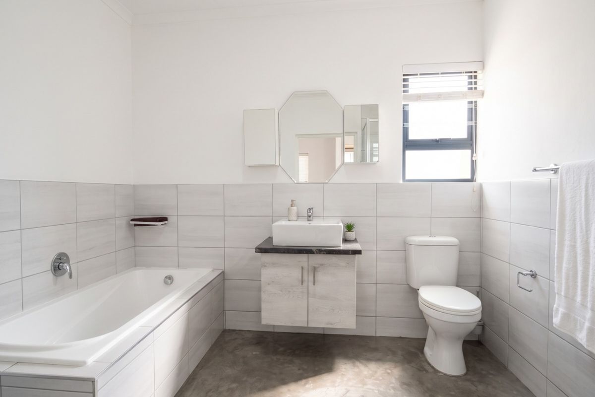 Modern bathroom featuring a built-in bathtub, wall-mounted vanity with vessel sink, toilet, and neutral tiled walls with polished concrete flooring.