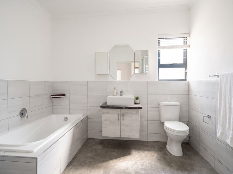 Modern bathroom featuring a built-in bathtub, wall-mounted vanity with vessel sink, toilet, and neutral tiled walls with polished concrete flooring.