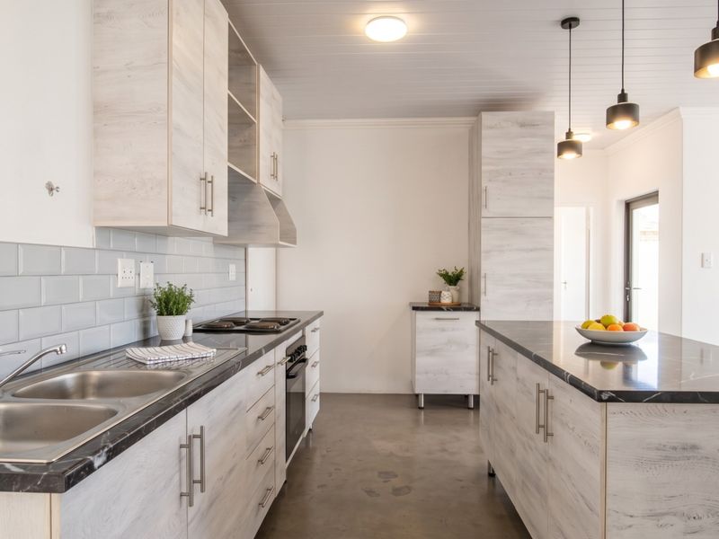 Modern kitchen featuring light wood-grain cabinetry, stone countertops, a central island, subway tile backsplash, and polished concrete flooring with contemporary pendant lighting.