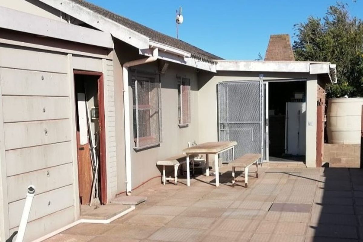 Rear exterior view of the property featuring a paved patio area, security gates, and a water storage tank.