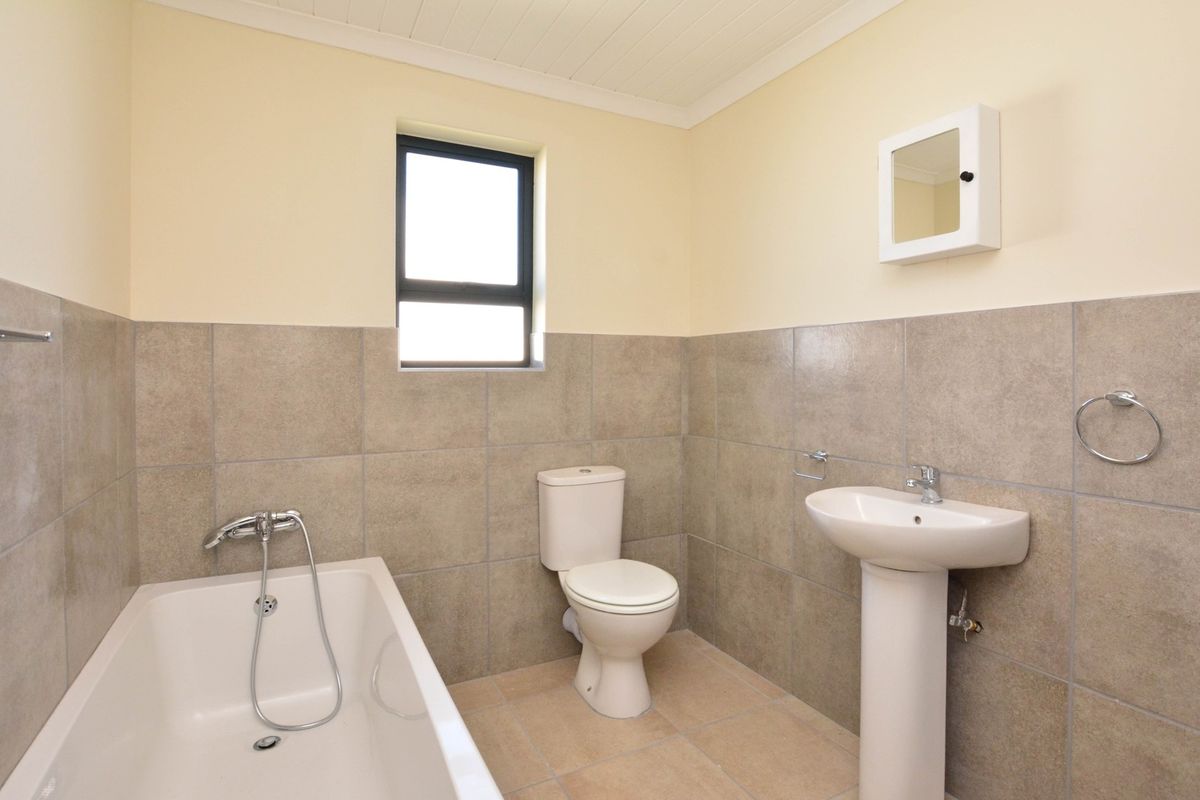 A functional bathroom featuring a standard bathtub, pedestal basin, and toilet with neutral wall tiling and a small window for natural light.