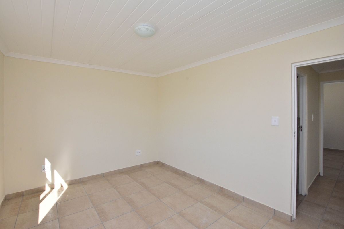 A clean, empty bedroom featuring neutral tiled flooring, a white tongue-and-groove ceiling, and a doorway leading to an adjacent space.
