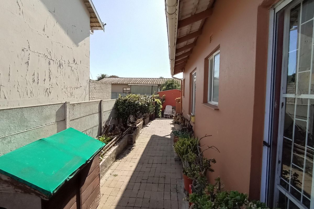 A narrow side walkway featuring paved flooring, bordered by a boundary wall and the side elevation of the house.