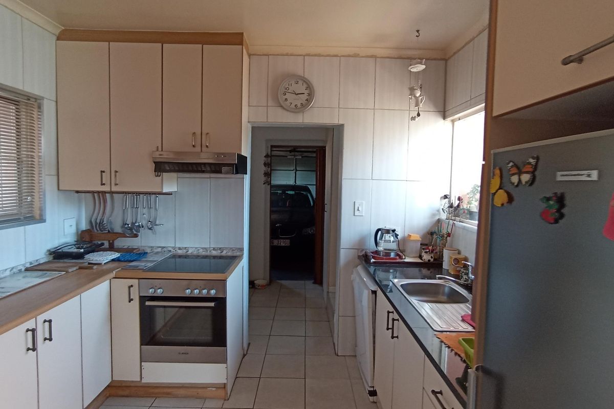 A functional kitchen featuring built-in cabinetry, a stainless steel oven with hob, extractor fan, and a stainless steel sink with tiled splashbacks.
