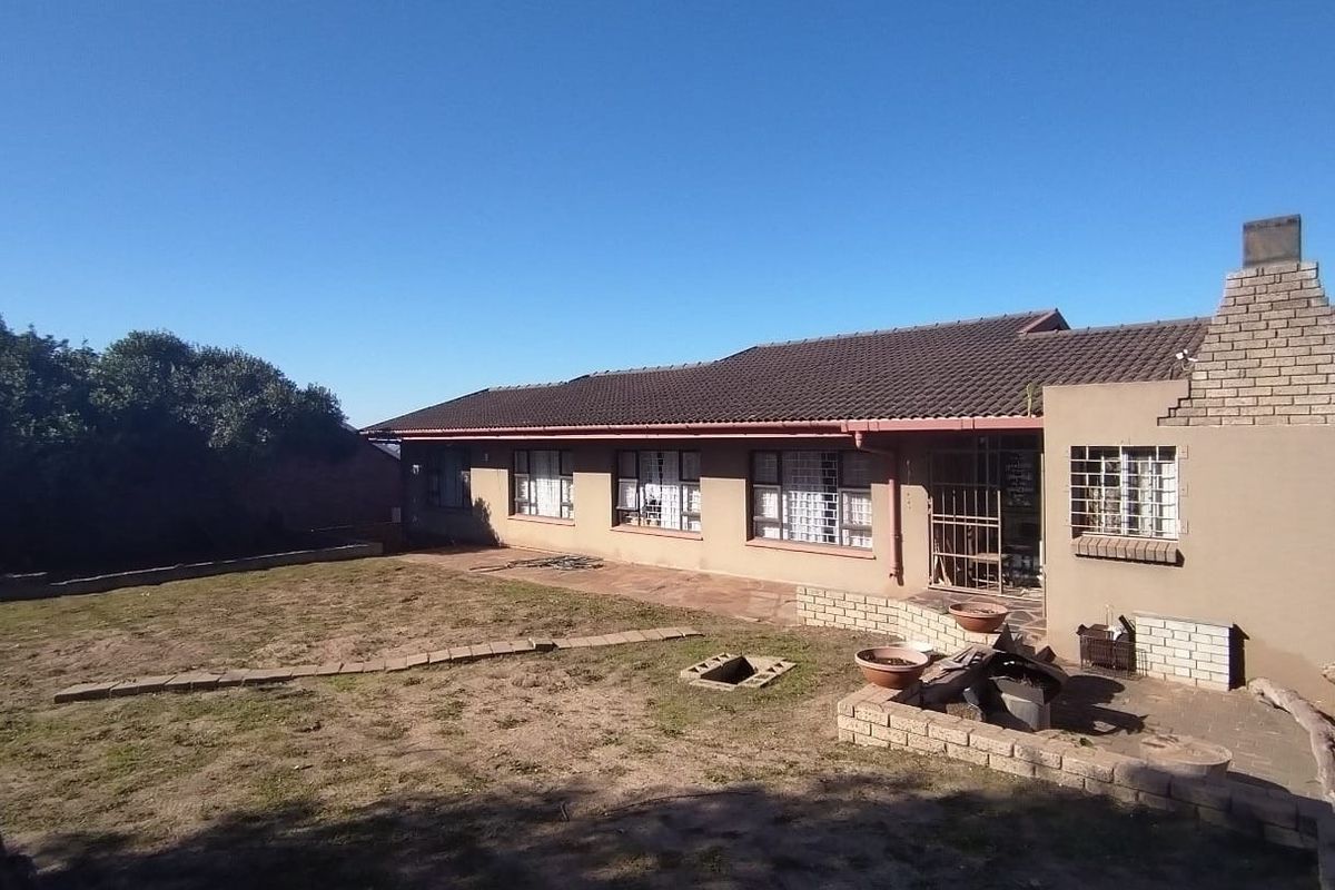 Rear view of the house featuring a tiled roof, brick chimney, paved patio area, and a spacious backyard.