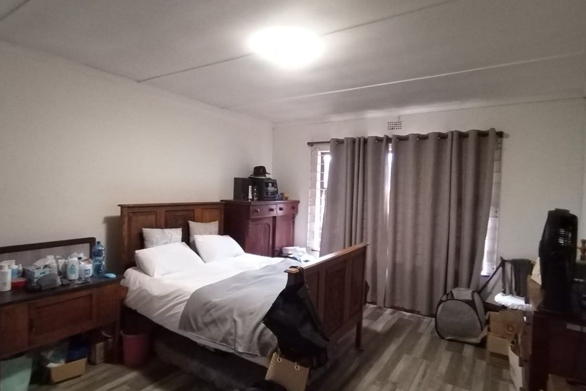 A spacious bedroom featuring wood-look laminate flooring, a central ceiling light, and sliding door access to the exterior.