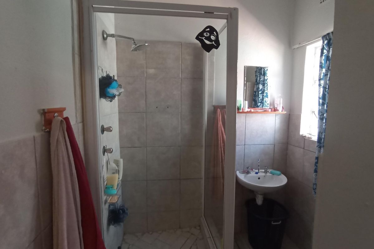 A functional bathroom featuring a glass-enclosed shower stall with tiled walls and a wall-mounted pedestal basin.