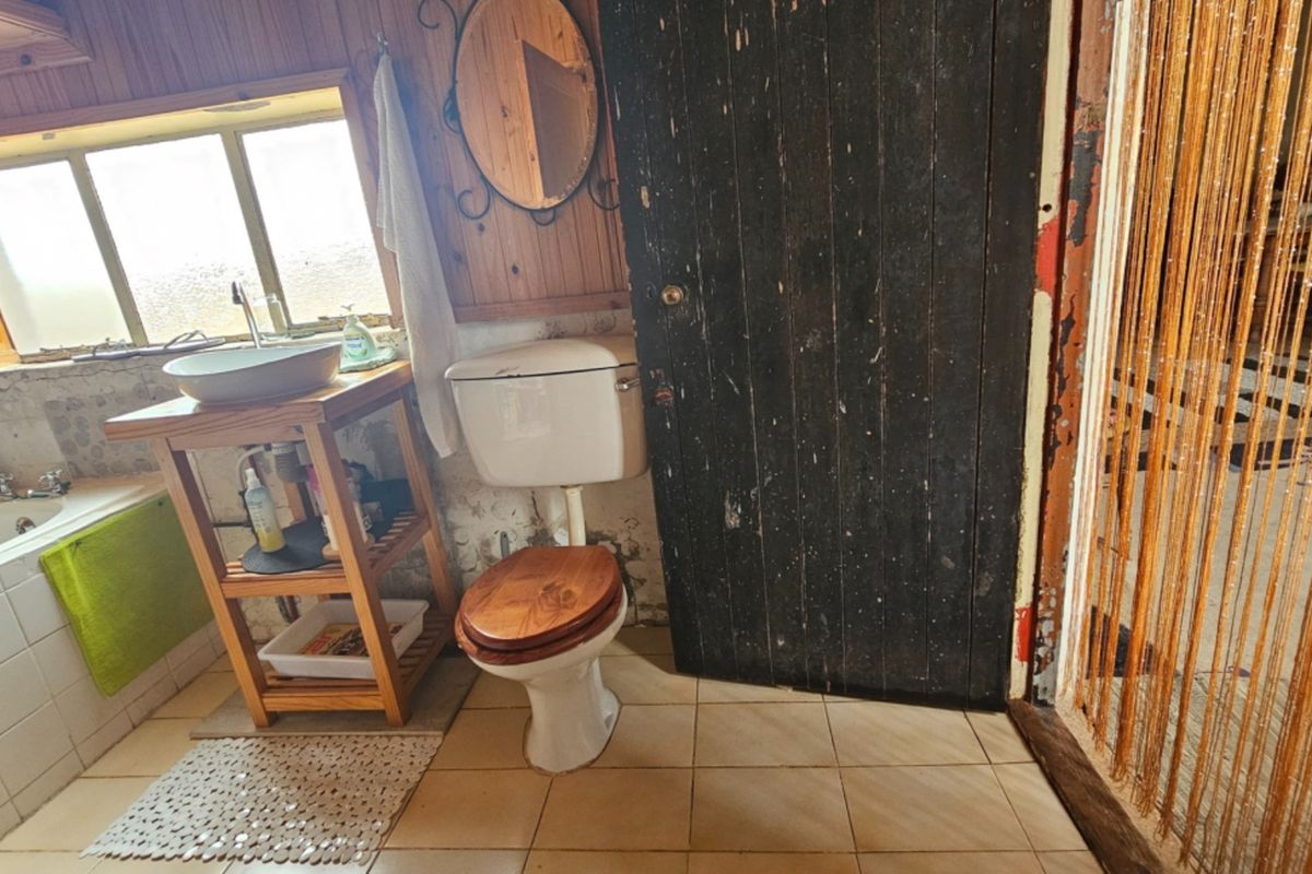 A dated bathroom featuring timber wall paneling, a vessel sink, and a ceramic bathtub, requiring significant cosmetic updates and repairs to finishes.