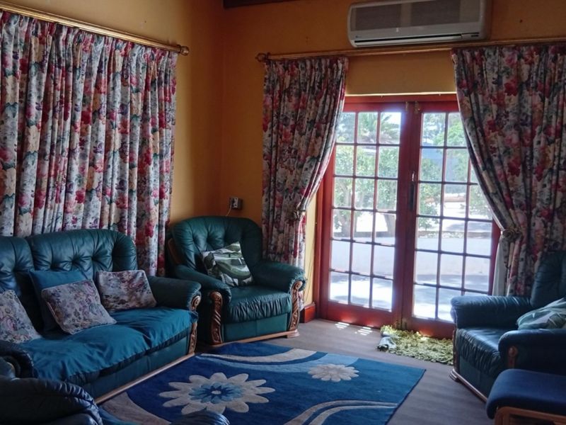 A living room featuring timber flooring, a wall-mounted air conditioning unit, and double french doors providing access to the outdoor area.