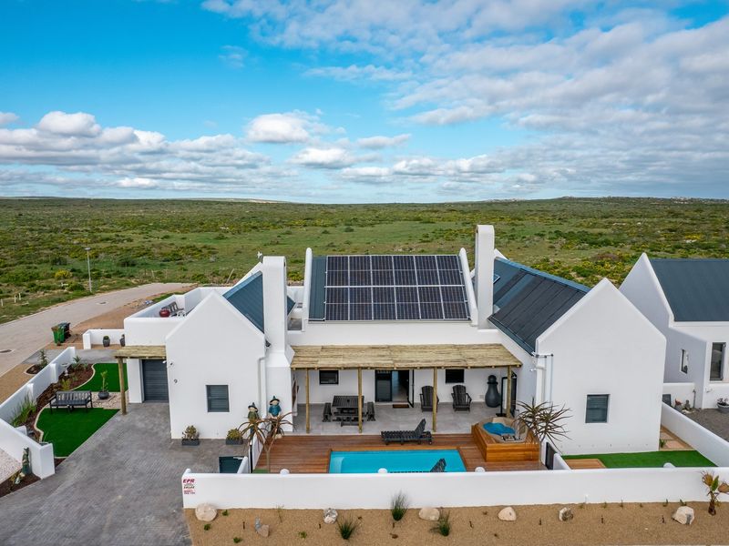 Aerial view of a modern house featuring a swimming pool, timber deck, covered patio, and roof-mounted solar panels set in a rural landscape.