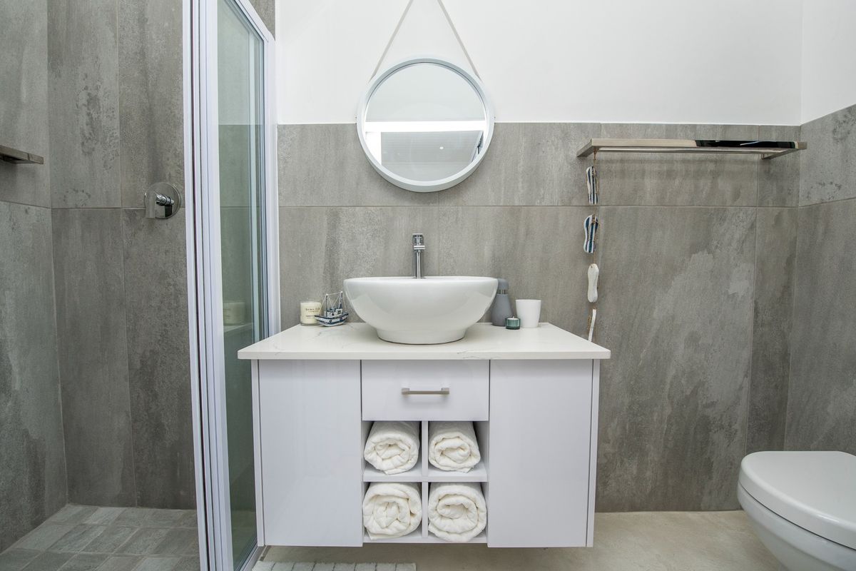 Modern bathroom featuring a wall-mounted vanity with vessel sink, walk-in shower, wall-hung toilet, and contemporary grey porcelain wall tiling.