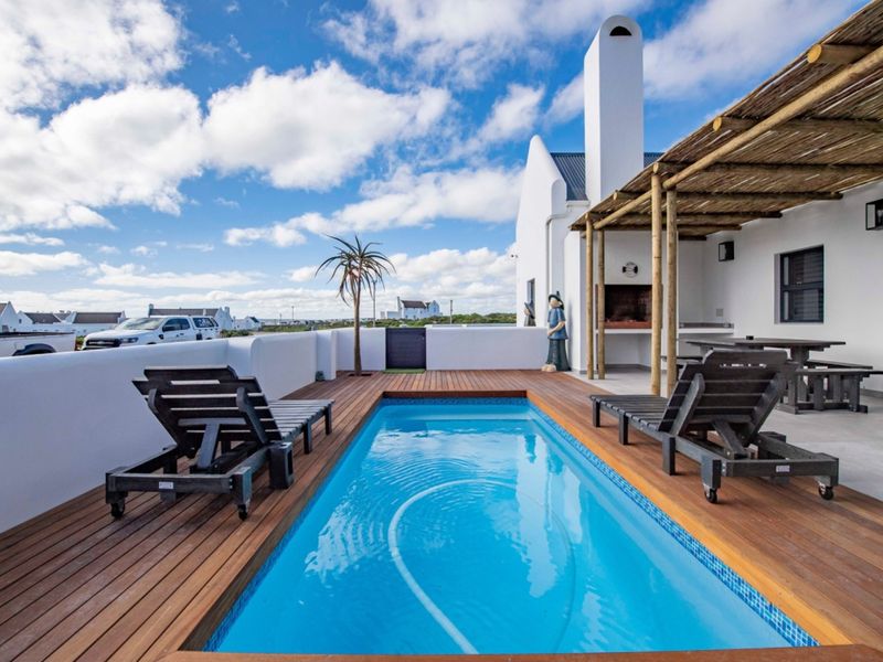 Outdoor pool area featuring timber decking, a built-in braai, and a covered pergola, perfect for entertaining.