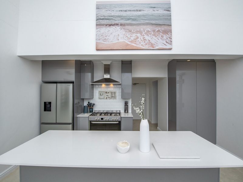 Modern kitchen featuring a central island, sleek grey cabinetry, subway tile backsplash, and a stainless steel gas stove with extractor fan.