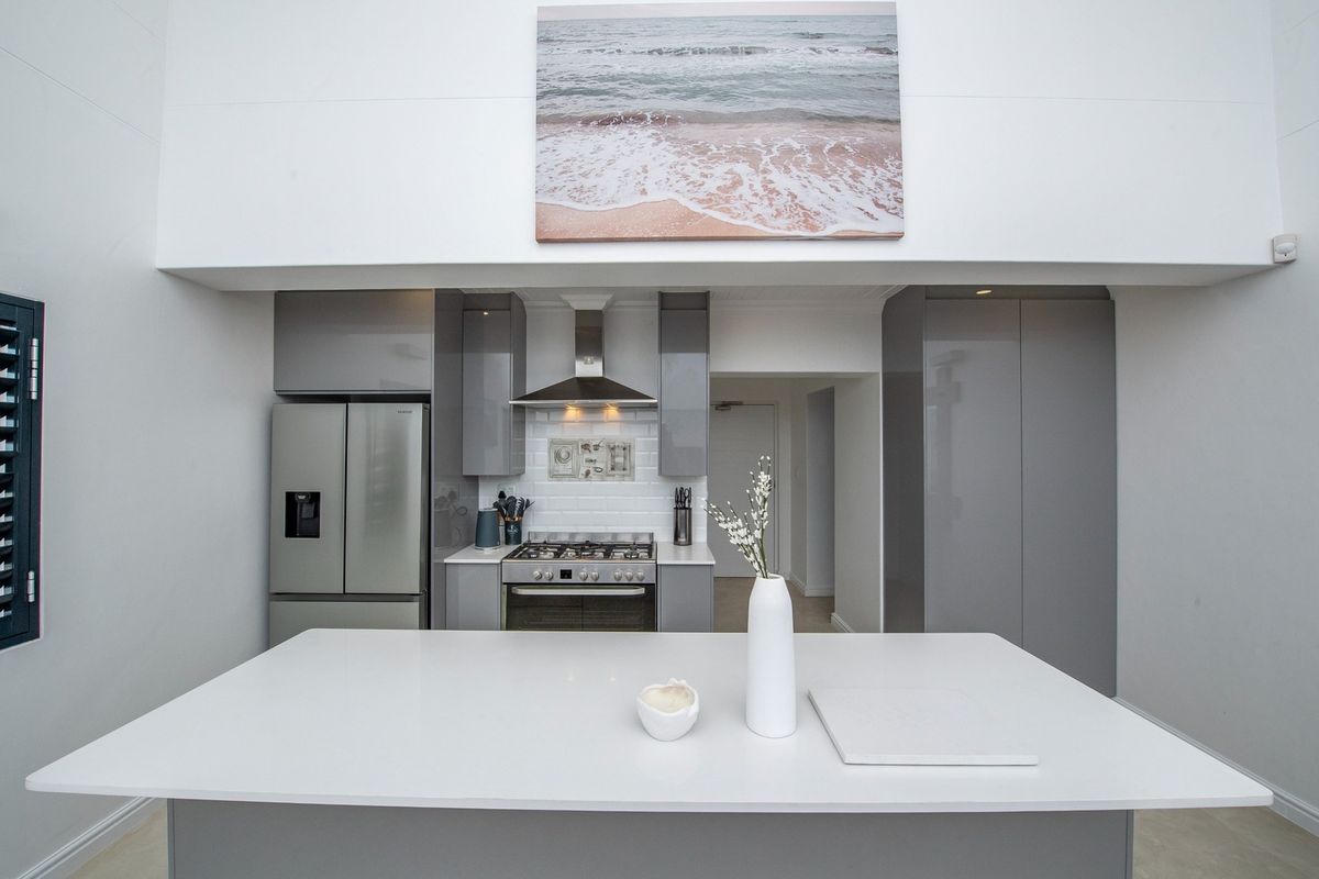 Modern kitchen featuring a central island, sleek grey cabinetry, subway tile backsplash, and a stainless steel gas stove with extractor fan.