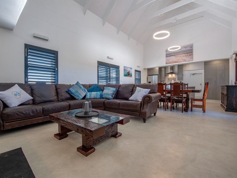 Spacious open-plan living and dining area featuring high vaulted ceilings with exposed rafters, polished concrete floors, and a modern integrated kitchen.