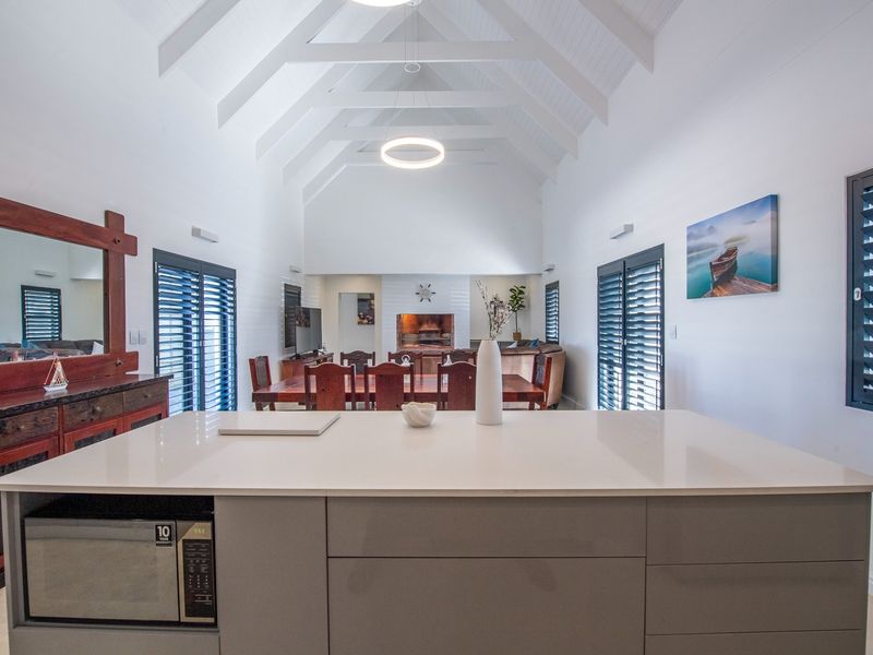 Spacious open-plan living and dining area featuring a modern kitchen island, vaulted ceilings with exposed rafters, and a cozy fireplace.