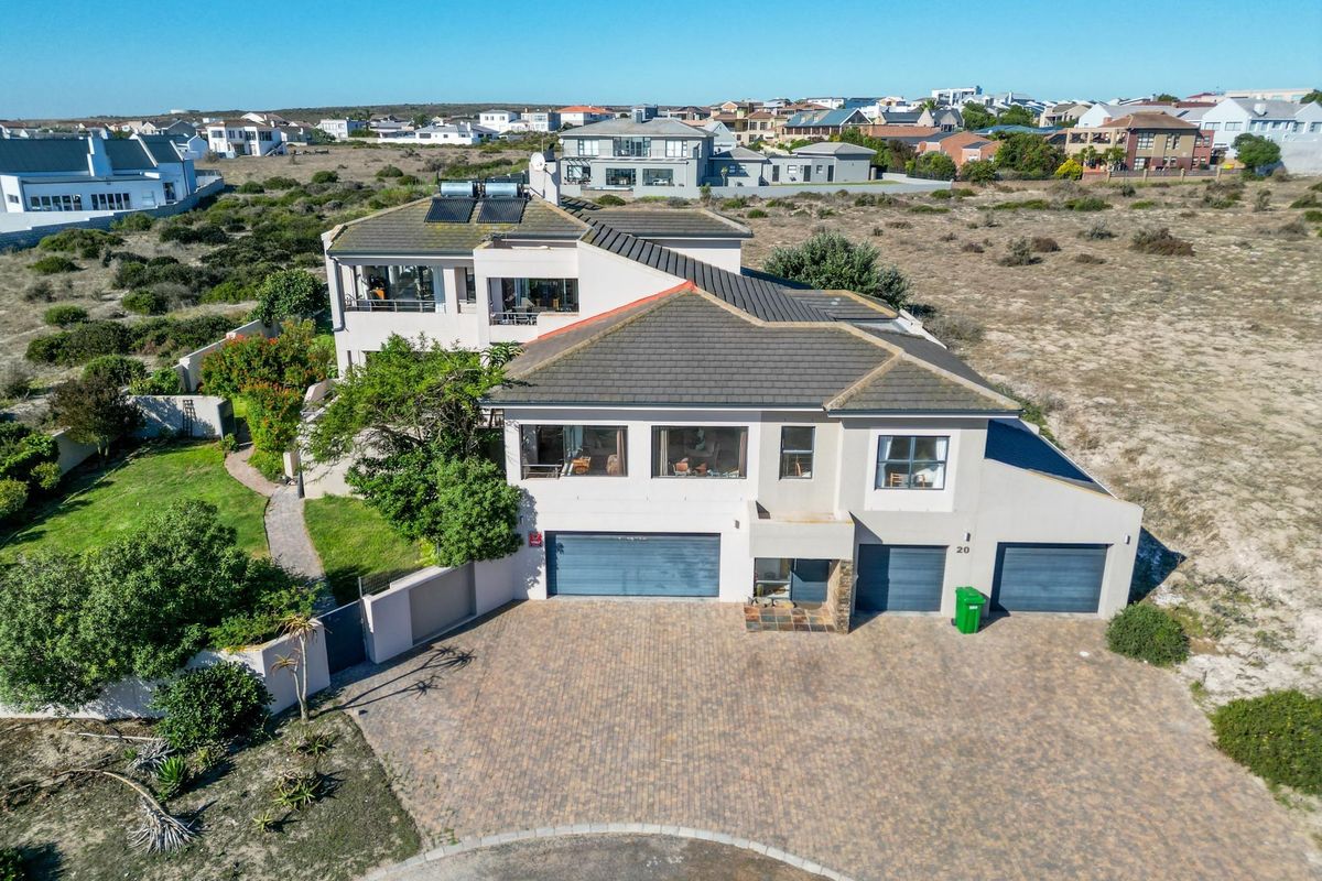 Aerial view of a multi-level residential property featuring a triple garage, paved driveway, and solar water heating panels on a tiled roof.