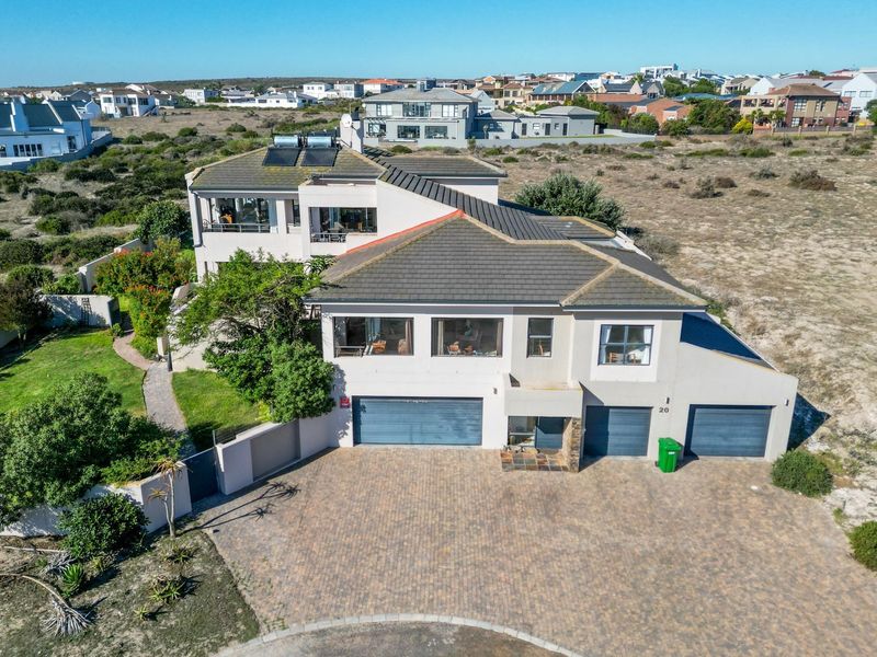 Aerial view of a multi-level residential property featuring a triple garage, paved driveway, and solar water heating panels on a tiled roof.