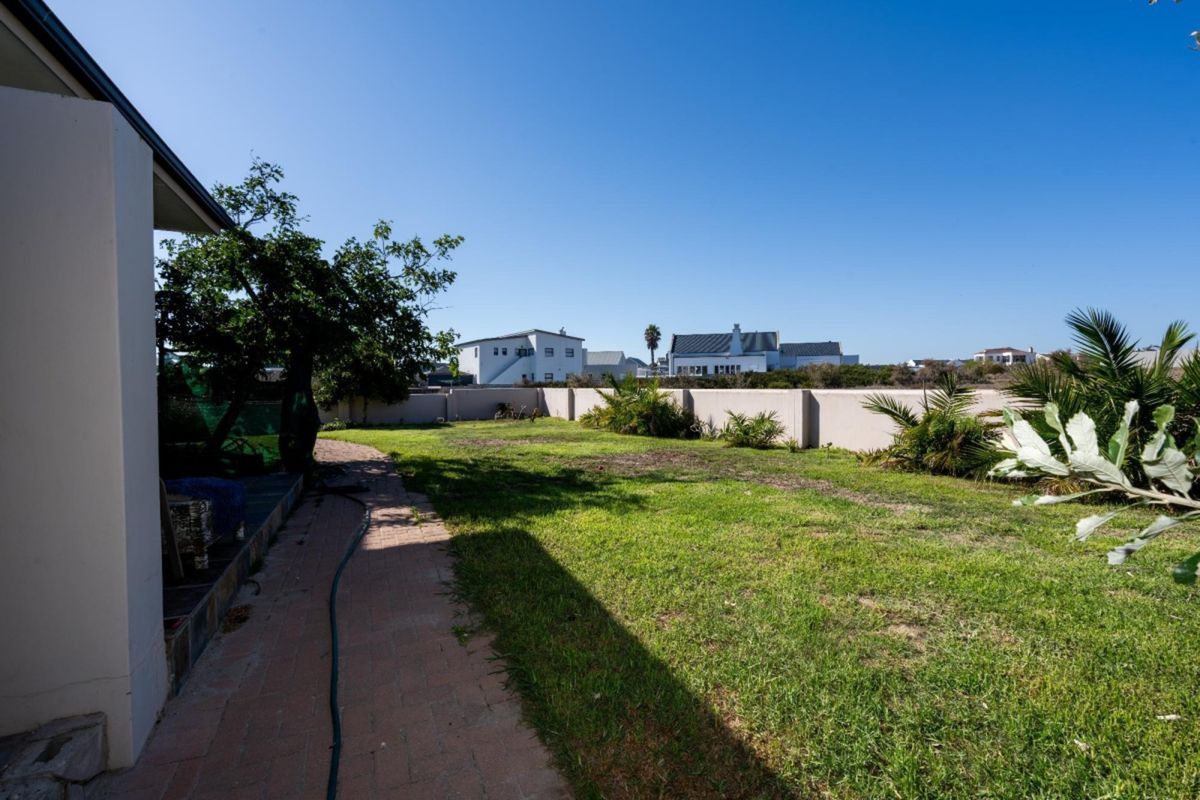 A spacious rear garden featuring a paved walkway, established lawn, and perimeter boundary walls, offering a private outdoor space.