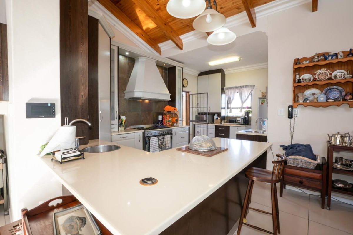 Spacious kitchen featuring a large central island with stone countertops, built-in oven, gas hob, extractor fan, and exposed timber ceiling beams.