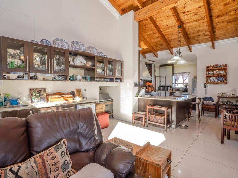 Spacious open-plan living and kitchen area featuring vaulted ceilings with exposed timber beams, tiled flooring, and a functional kitchen island.