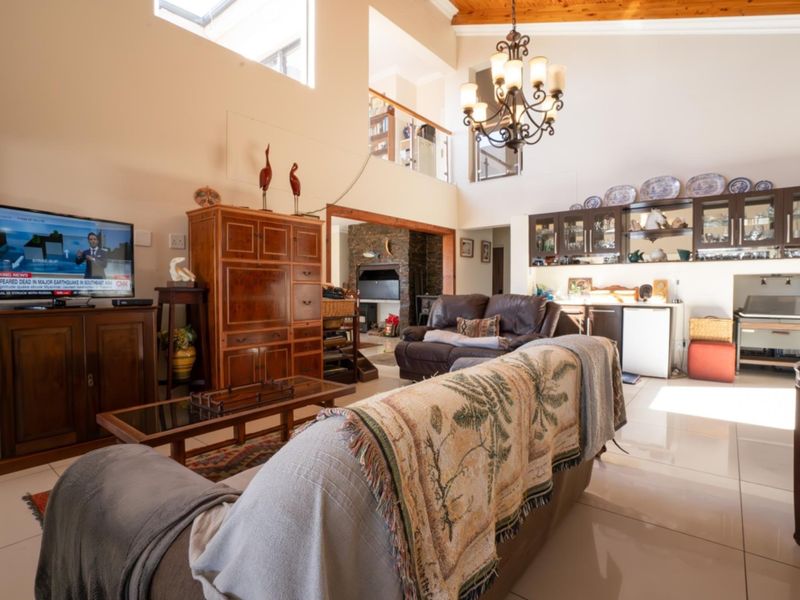 Spacious open-plan living area featuring high vaulted ceilings with exposed timber beams, tiled flooring, a stone fireplace, and a mezzanine level overlooking the space.