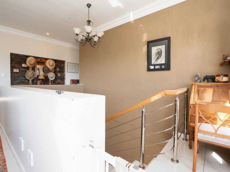 A bright landing area featuring a modern stainless steel balustrade with a wooden handrail, tiled flooring, and a decorative stone feature wall.
