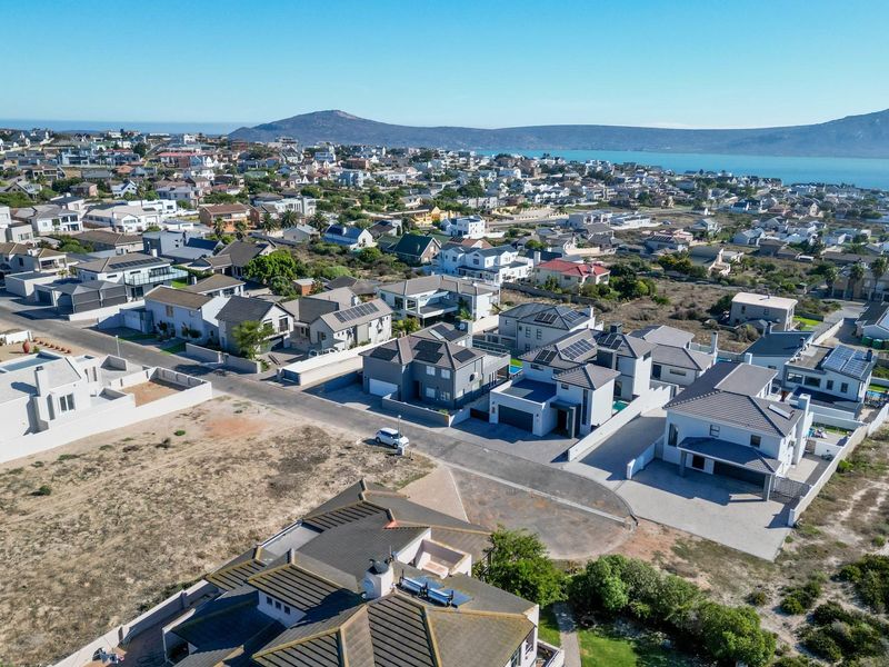 An aerial view of a coastal residential neighborhood featuring modern homes with tiled roofs, solar panels, and paved driveways overlooking the bay.