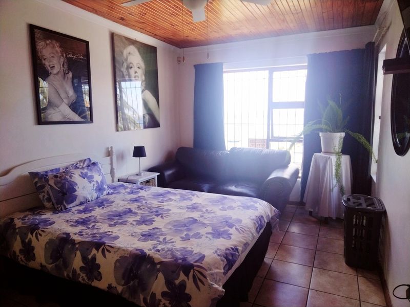 A bedroom featuring tiled flooring and a timber tongue and groove ceiling with an integrated ceiling fan and security bars on the window.