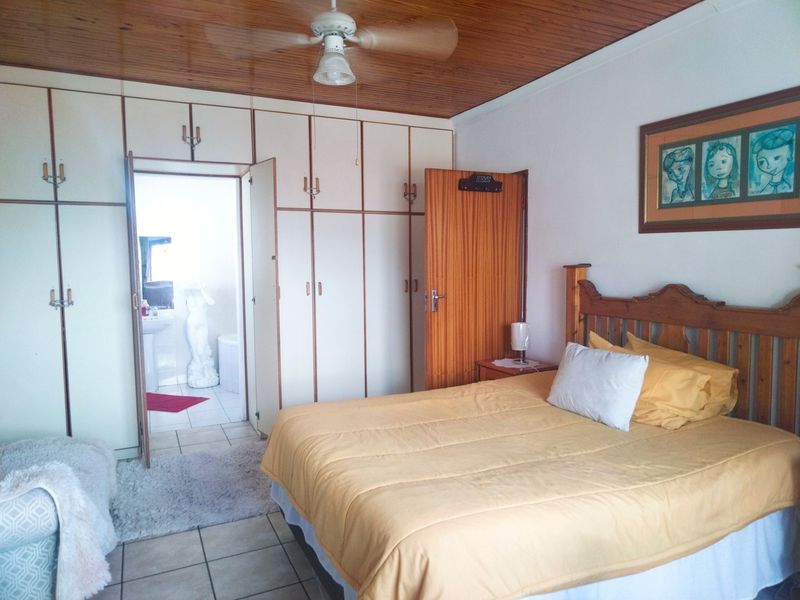 Bedroom featuring built-in cupboards, tiled flooring, and a timber ceiling, with an adjoining bathroom visible through the doorway.