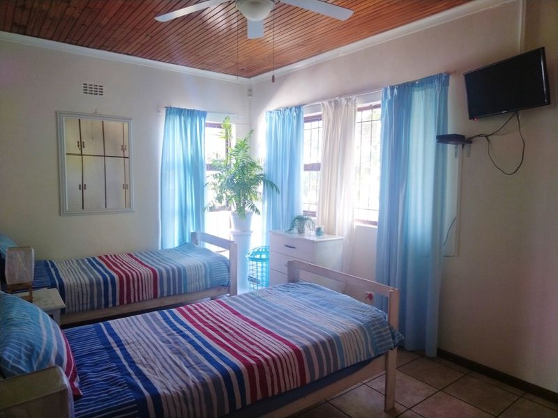 A bedroom featuring a timber-paneled ceiling, ceiling fan, and tiled flooring, with natural light entering through windows fitted with security bars.