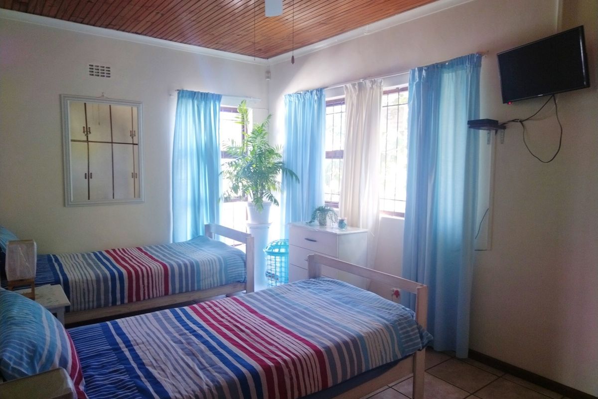 A bedroom featuring a timber-paneled ceiling, ceiling fan, and tiled flooring, with natural light entering through windows fitted with security bars.
