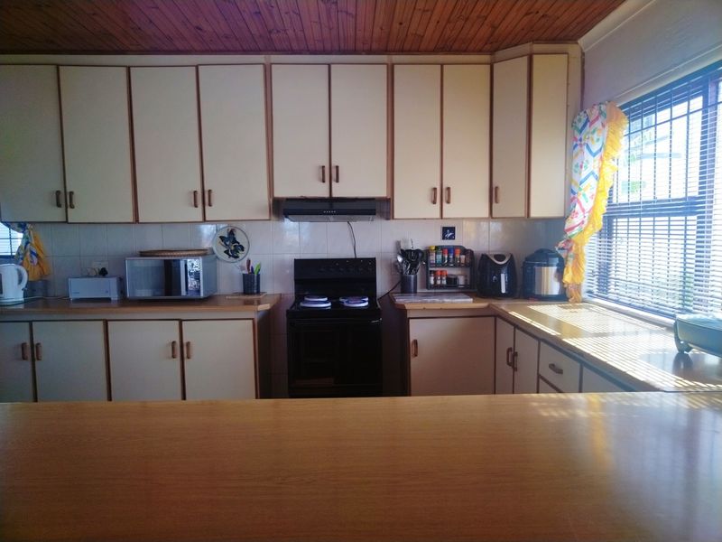 A functional kitchen featuring timber ceiling paneling, laminate countertops, and ample built-in cabinetry, offering a classic layout with natural light from the side window.