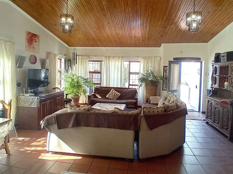 Spacious living room featuring a warm timber tongue and groove ceiling, terracotta floor tiles, and natural light through multiple windows with security bars.