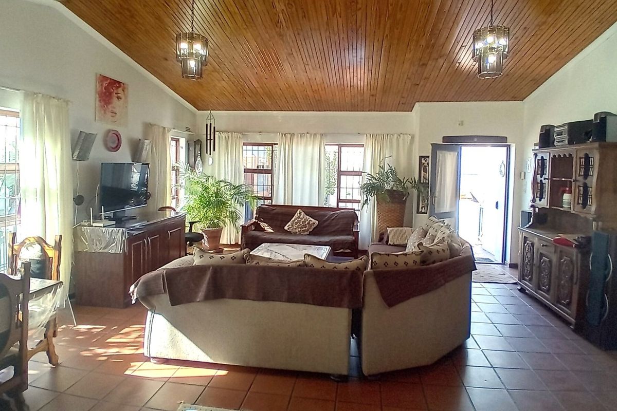 Spacious living room featuring a warm timber tongue and groove ceiling, terracotta floor tiles, and natural light through multiple windows with security bars.