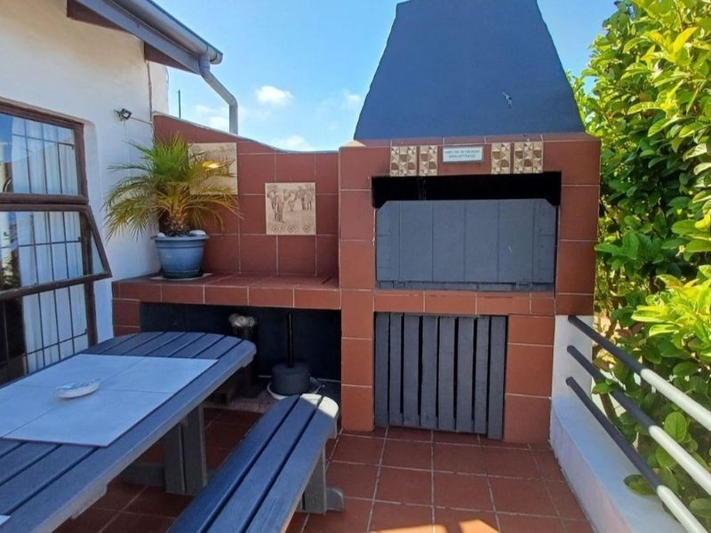 Outdoor patio area featuring a built-in braai, tiled flooring, and metal safety railing, ideal for alfresco dining and entertaining.