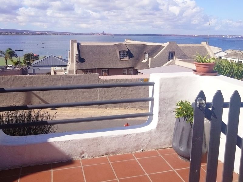 An elevated balcony featuring terracotta tiling, a solid masonry balustrade with metal railings, and expansive coastal views.