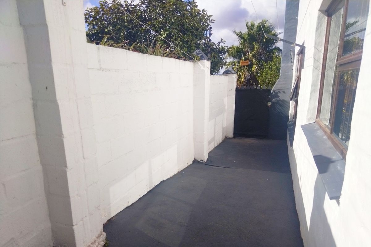 A side walkway featuring a painted concrete block boundary wall, electric fencing, and a secure gate leading to the rear of the property.