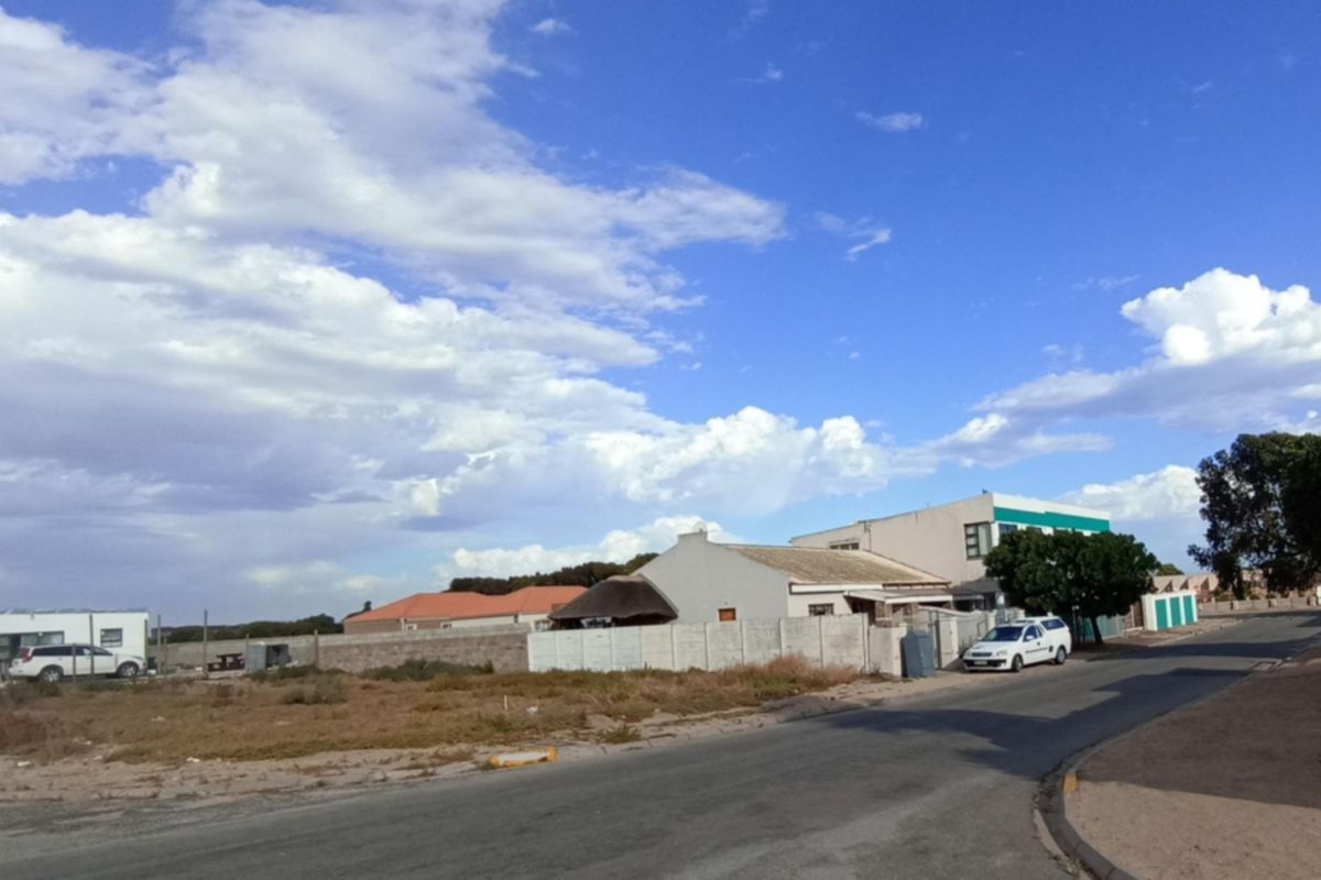 A street-level view of a vacant residential plot featuring a boundary wall and access to a paved road in a suburban neighborhood.