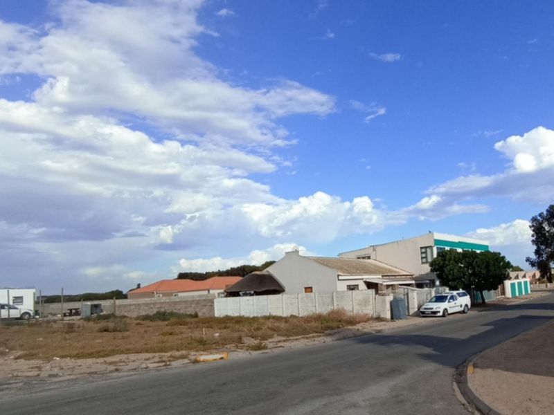 A street-level view of a vacant residential plot featuring a boundary wall and access to a paved road in a suburban neighborhood.