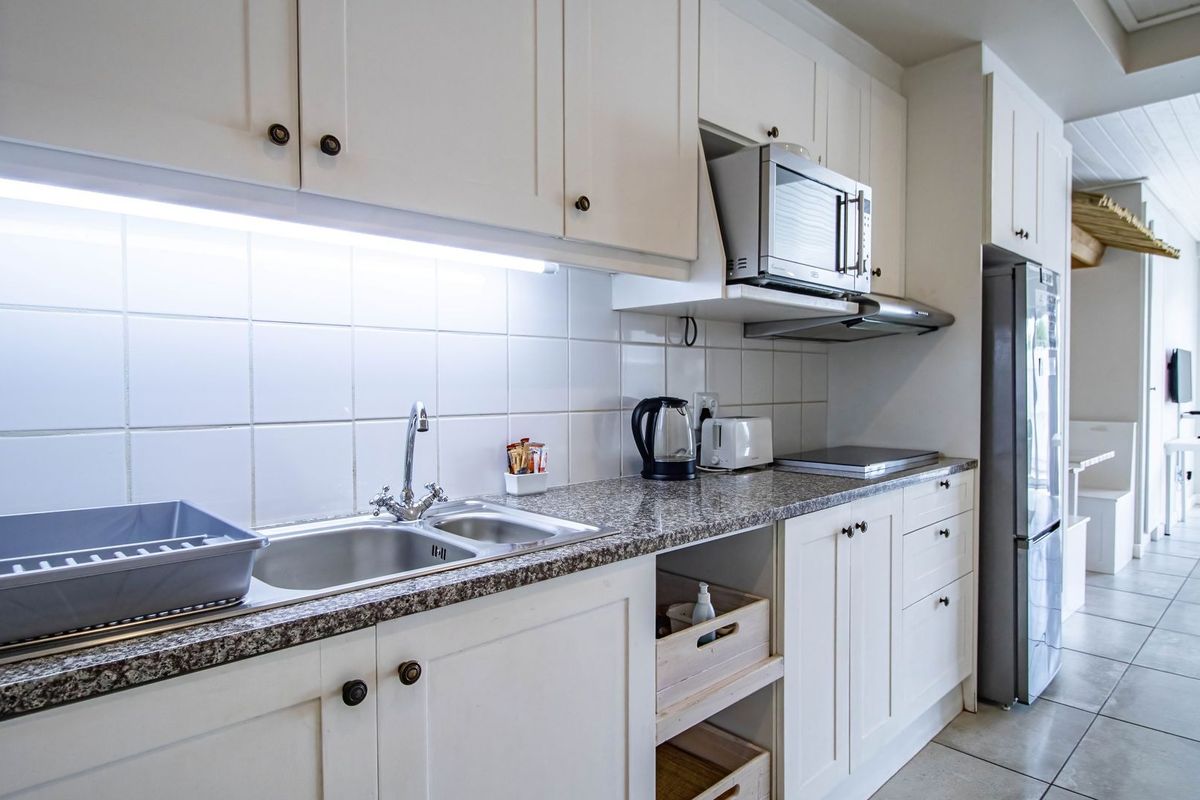 A functional kitchen featuring white shaker-style cabinetry, granite countertops, a double stainless steel sink, and integrated appliances including a microwave and extractor fan.