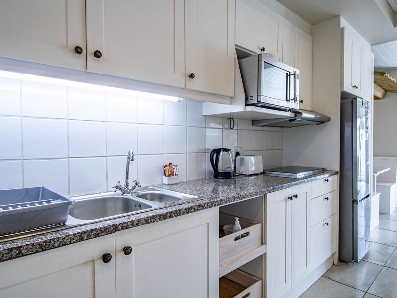 A functional kitchen featuring white shaker-style cabinetry, granite countertops, a double stainless steel sink, and integrated appliances including a microwave and extractor fan.