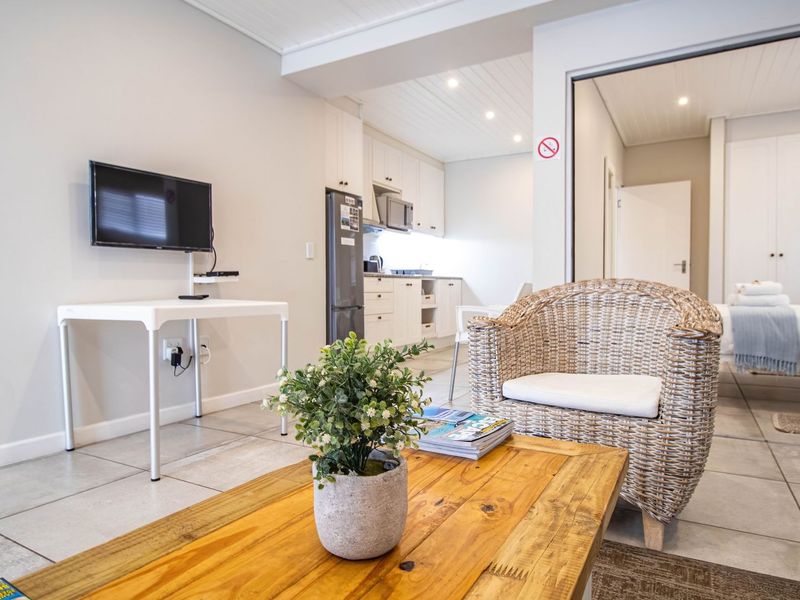 An open-plan living area featuring tiled floors, recessed lighting, and a compact kitchen, seamlessly flowing into an adjacent bedroom space.