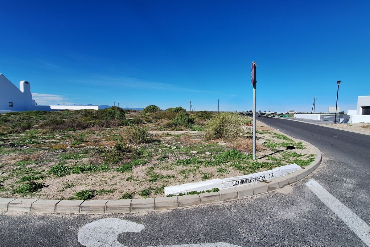 A street-level view of a vacant residential plot situated on a corner, featuring established road infrastructure and curbing.