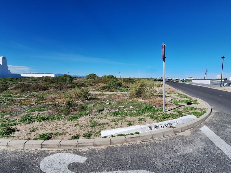 A street-level view of a vacant residential plot situated on a corner, featuring established road infrastructure and curbing.