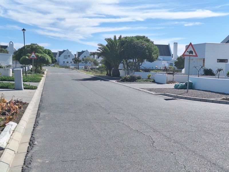 A view of a paved residential street within a well-maintained estate, featuring landscaped verges and surrounding white-walled residential properties.