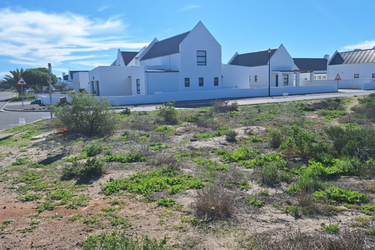 A vacant residential plot situated in a developed estate with paved street access and surrounding modern white homes.